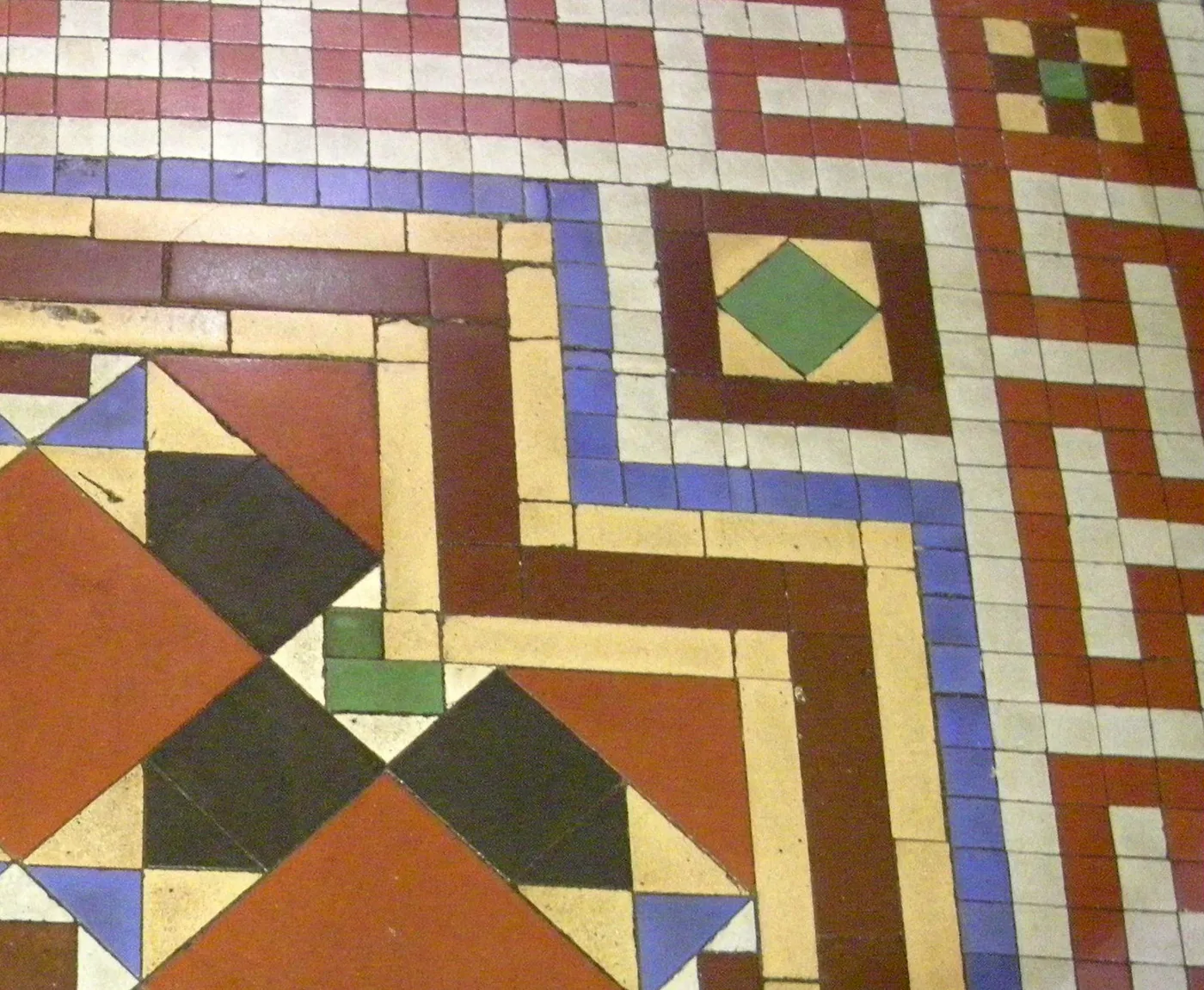 A Victorian encaustic tiled floor with a repeating geometric pattern in terracotta, cream and black
