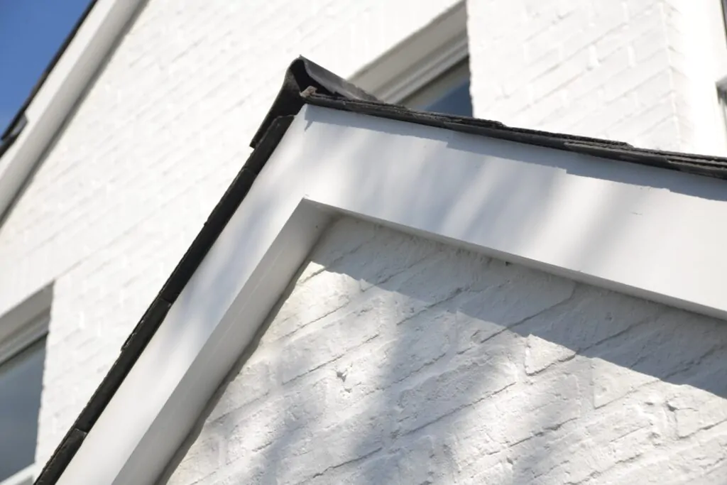 Close-up of a slanted black roof edge with white brick siding and sunlight casting shadows