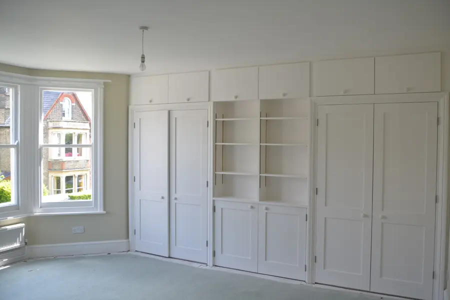 Bedroom wall of fitted wardrobes and shelving painted in white