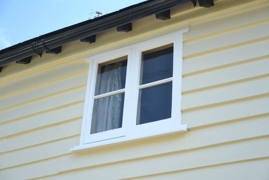 White-framed window on a pale yellow wooden-panelled house exterior