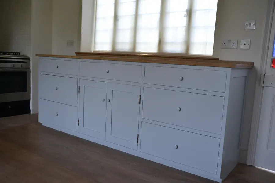 Long run of kitchen units resprayed in soft grey with oak worktop