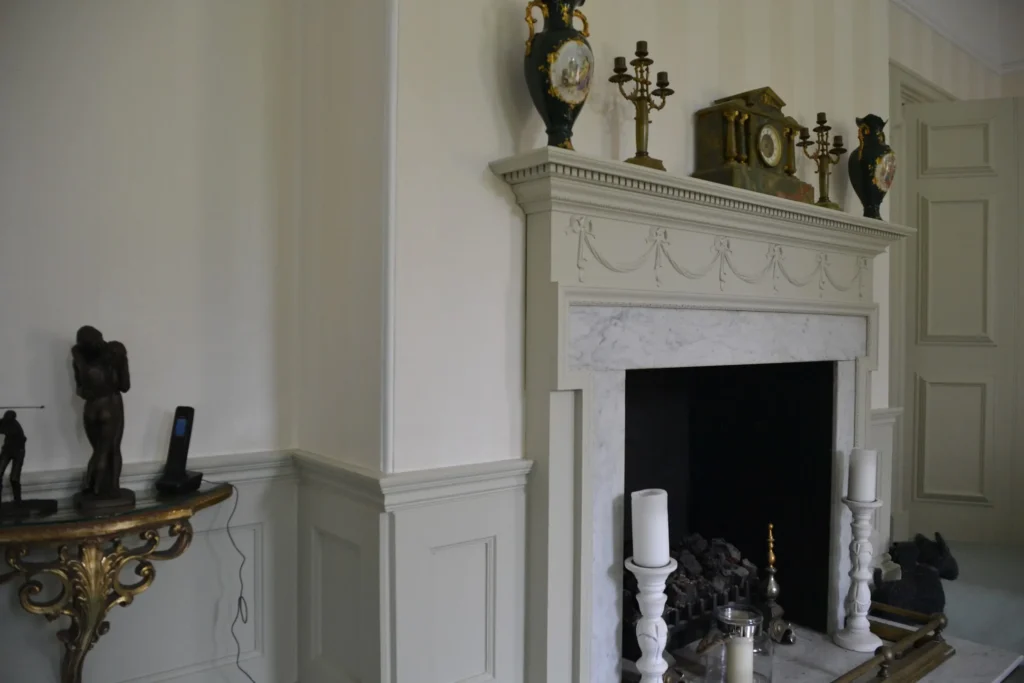 Elegant living room with a white marble fireplace, ornate clock, vases, and candelabra on the mantel.