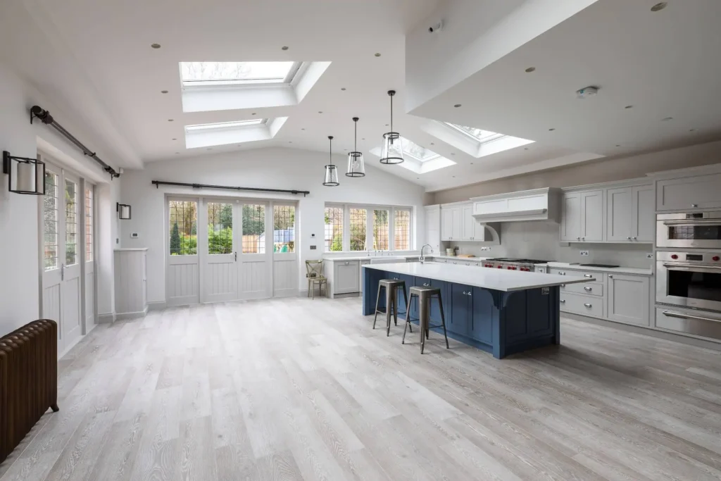 Spacious kitchen with light wood flooring, skylights, large island with stools, and white cabinetry.