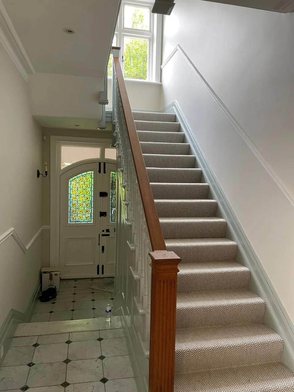 Period hallway with a stained-glass window beside the decorated staircase