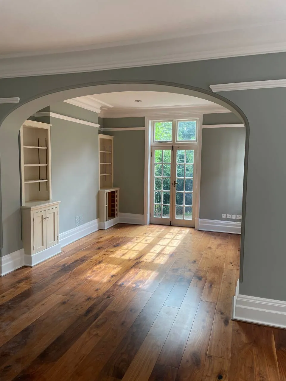 Sage-green period room with an archway and painted built-in cabinetry