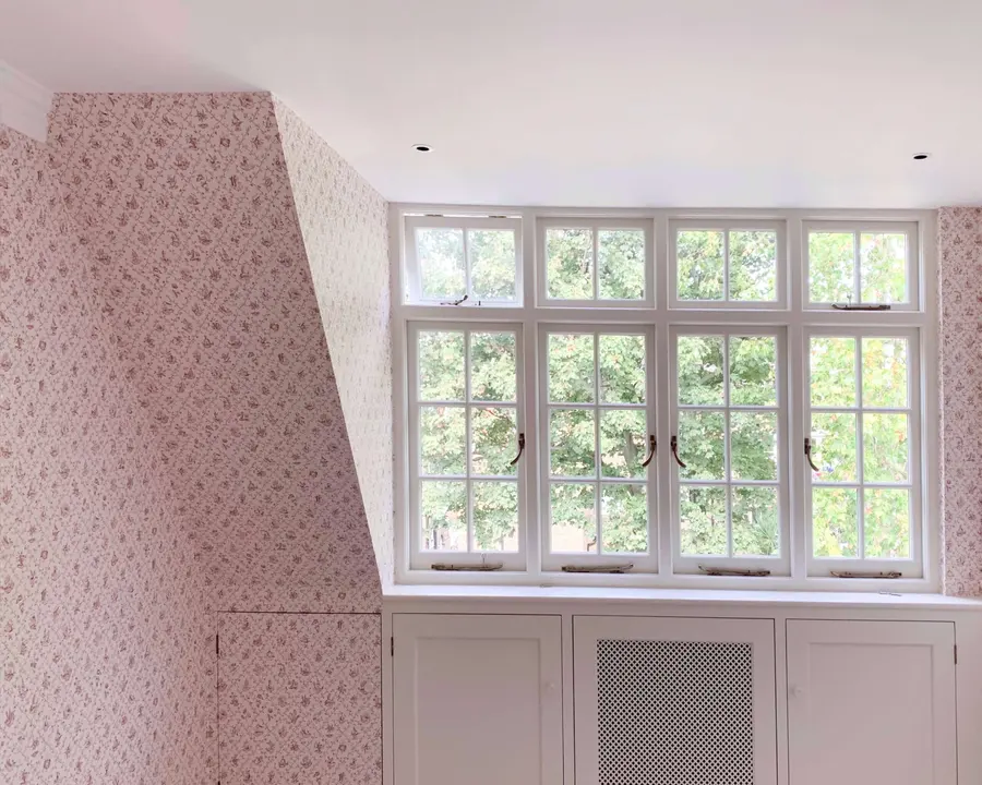 Soft floral wallpaper hung in a bedroom around a dormer window