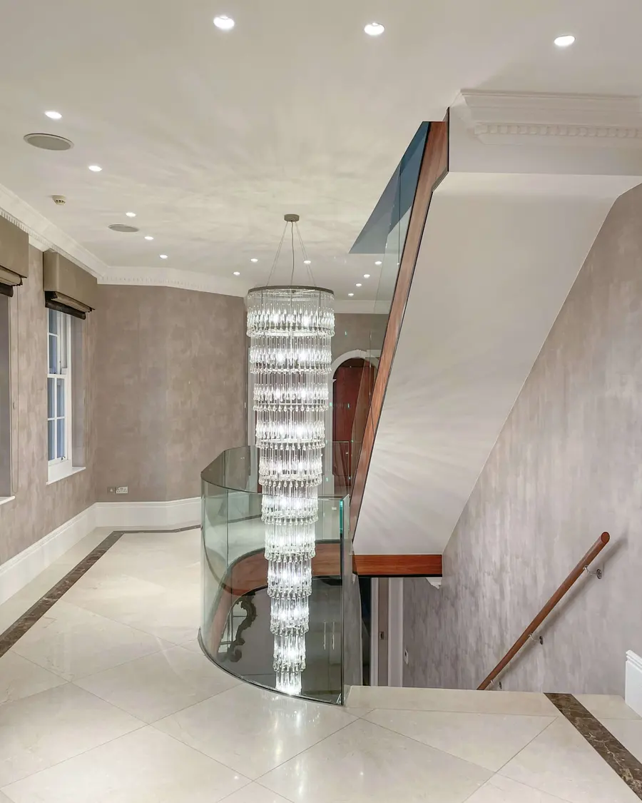 Grand hallway wallpapered beneath a curved staircase and chandelier