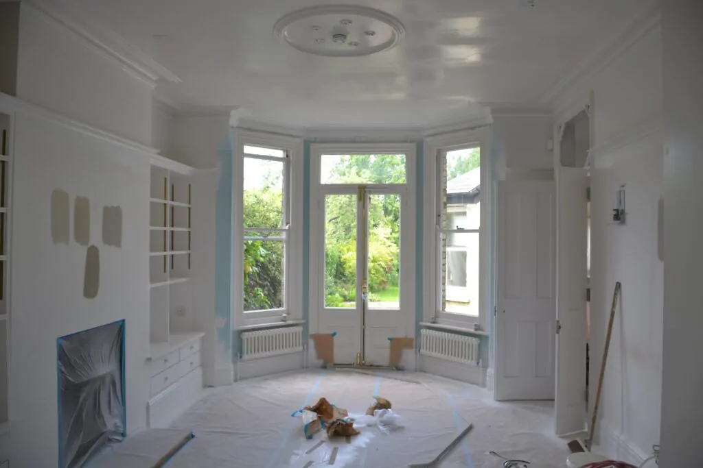 Room under renovation with large bay windows and paint samples on walls